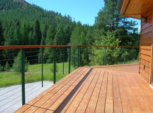 Green metal railing posts and wood top rail complement the forest view