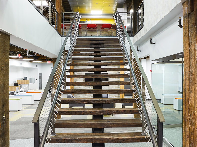 Mono-stringer staircase with weathered, industrial look located in an office space with open beam construction.