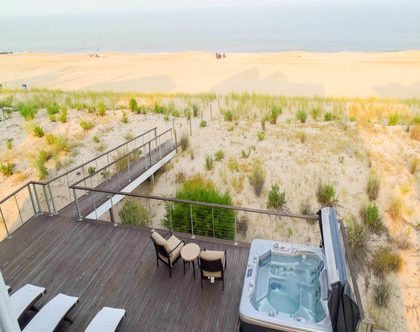 Large deck facing the beach with cable railing, hot tub, and lounge area.