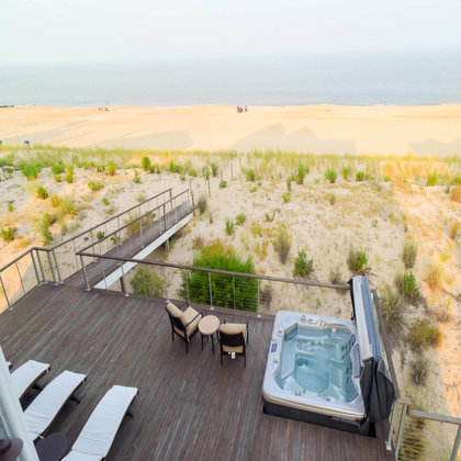 Large deck facing the beach with cable railing, hot tub, and lounge area.