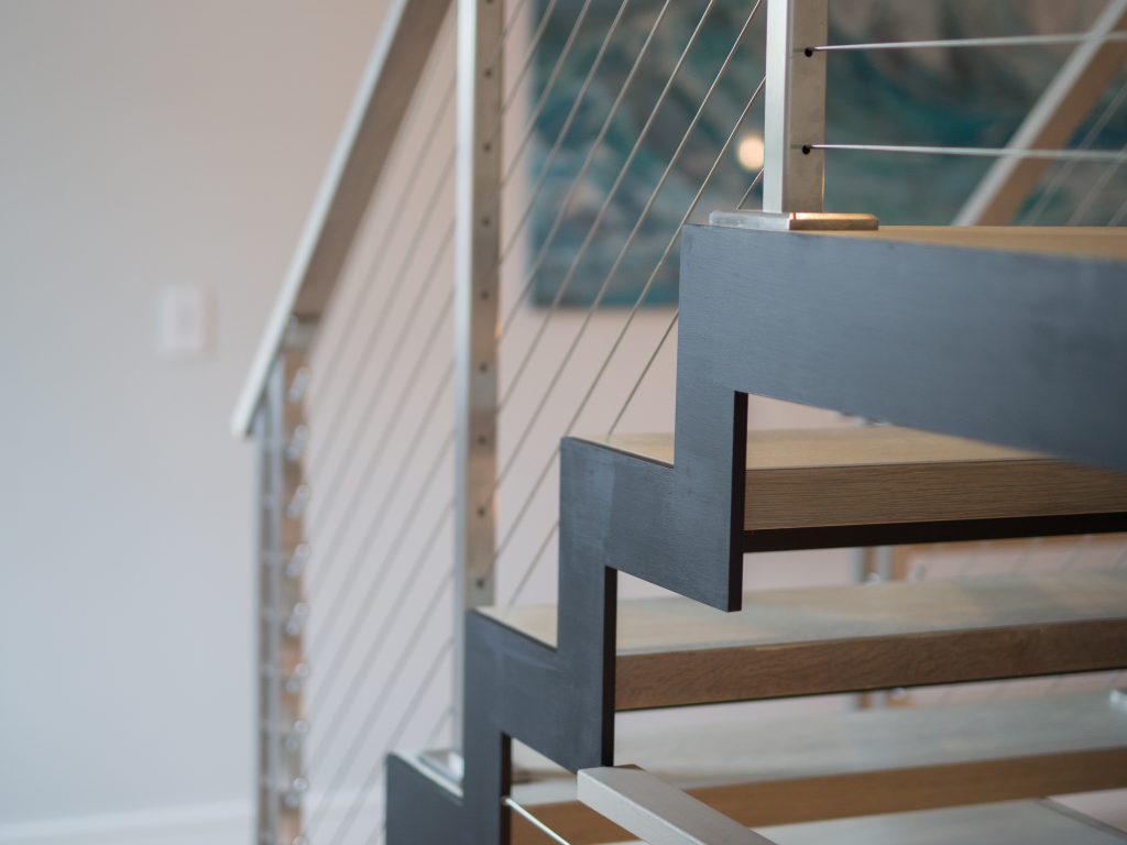 Zig Zag double stringer staircase with wood treads, stainless steel railing posts and cable railing. LED lighting on the treads.