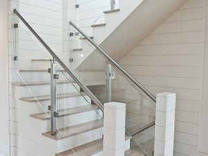 Nautical stair design idea with stainless rails, glass infill and shiplap white walls.