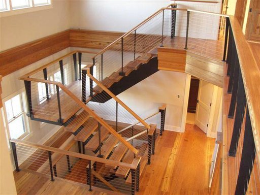 Custom tapered railing posts in black with cable railings. Wood stair treads, and handrails match the flooring.