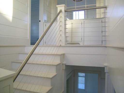 Round stainless steel handrails combined with cable railings that connect to wood posts for a nautical aesthetic