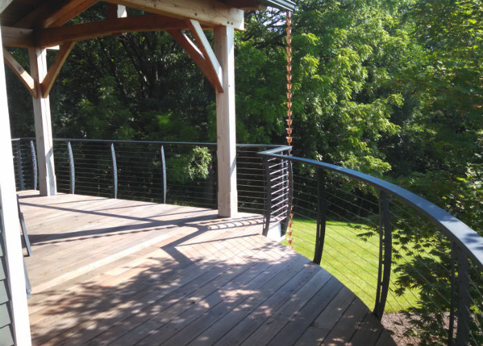 Timber style home with curved deck and cable railing there is rain chain used for water drainage