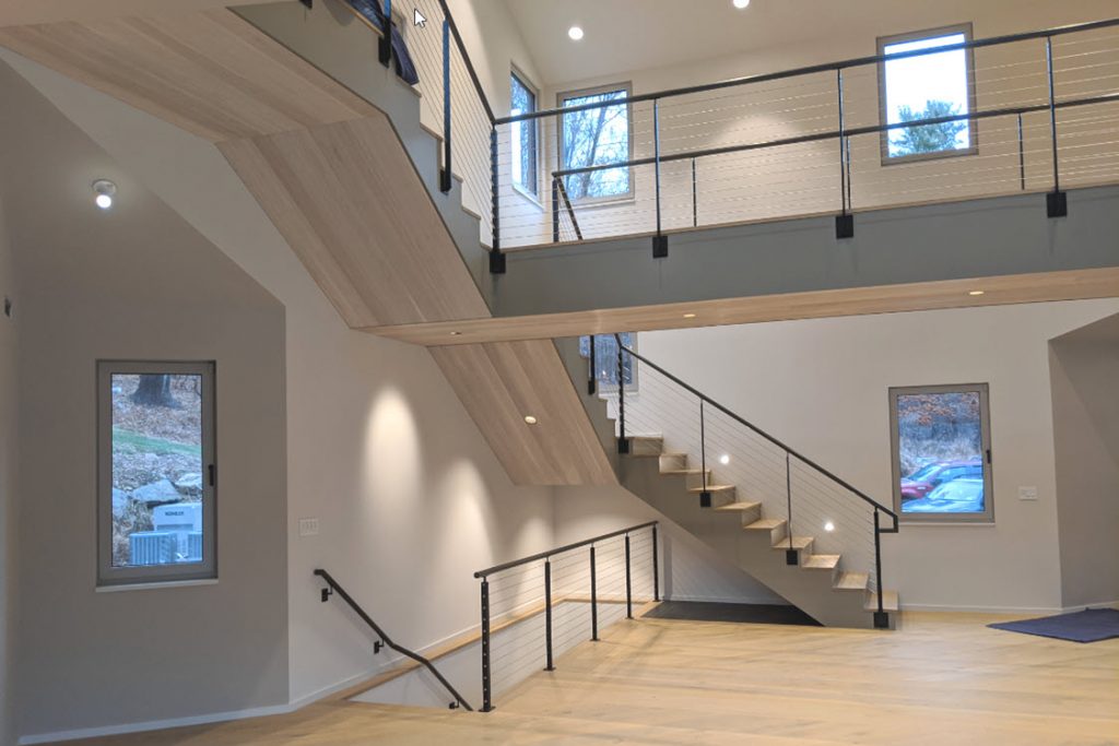 Minimalist railing on modern home with catwalk over looking living room. This narrow bridge allows for large open ceilings.