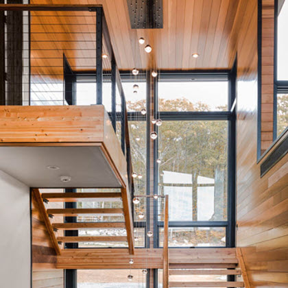 Interior of home with black cable railing on stairs, and wood ceilings with large windows.