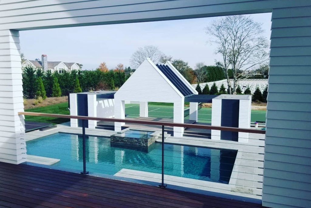 Covered master bedroom deck with stainless steel cable railing system and gray posts overlooking pool area.