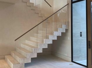 Glass railing slices through the stone tread. The steel support structure is hidden within the treads.