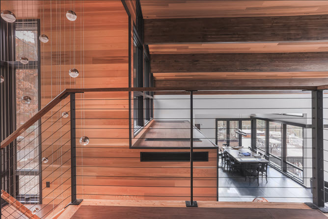 Black cable Railing on wood stairs on the interior of a home with wood panneling and high ceilings.