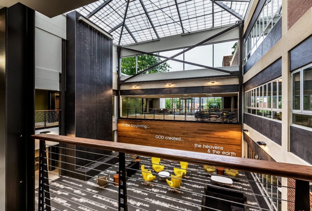 College atrium with wood wall, water feature wall and industrial railing system on balcony.