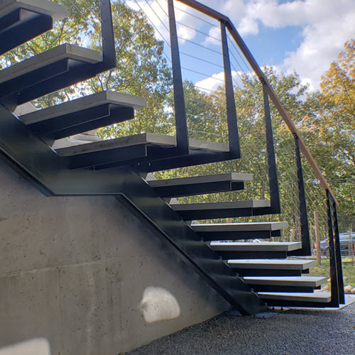 Cantilever exterior stairs with stringer along concrete wall and stone steps with cable railing.