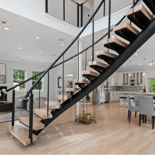 Curved round tube stair stringer with cable railing and wood steps shown in a homes great room entrance.
