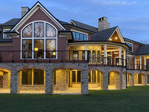 Curved decks with curved cable railings on traditional home with stone arch supports