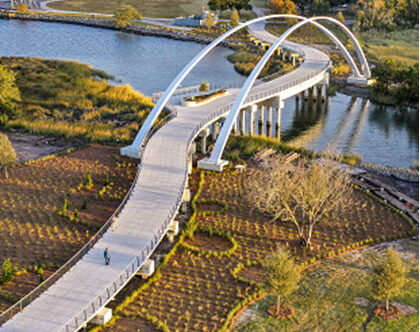 Sky view of concrete pedestrian bridge traversing the marsh with cable railings, viewing deck and massive concrete arches
