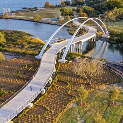 Sky view of concrete pedestrian bridge traversing the marsh with cable railings, viewing deck and massive concrete arches