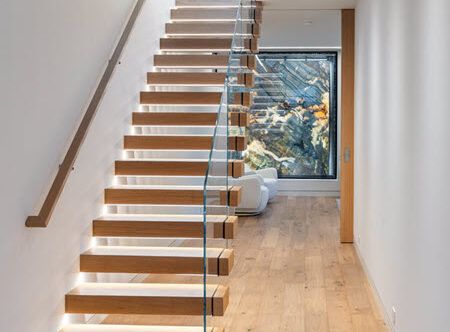 Modern lighted cantilever stair with wood treads and glass railing.