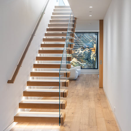 Modern lighted cantilever stair with wood treads and glass railing.