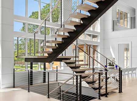 Floating stairs and landing with cable railings in open living space with floor to ceiling windows.