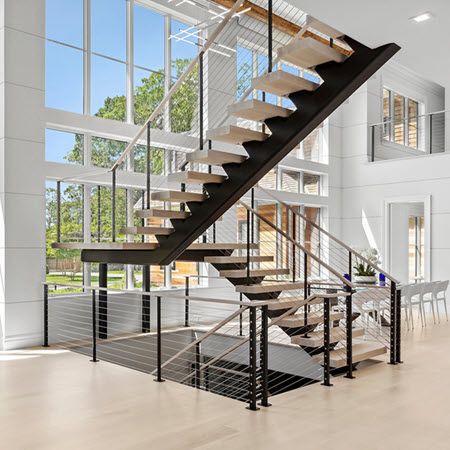 Floating stairs and landing with cable railings in open living space with floor to ceiling windows.