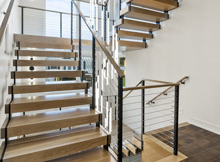 Double Stringer floating stair ascends three stories in a residential home. The stairs have wood treads and hanrails and there is a large chandelier.