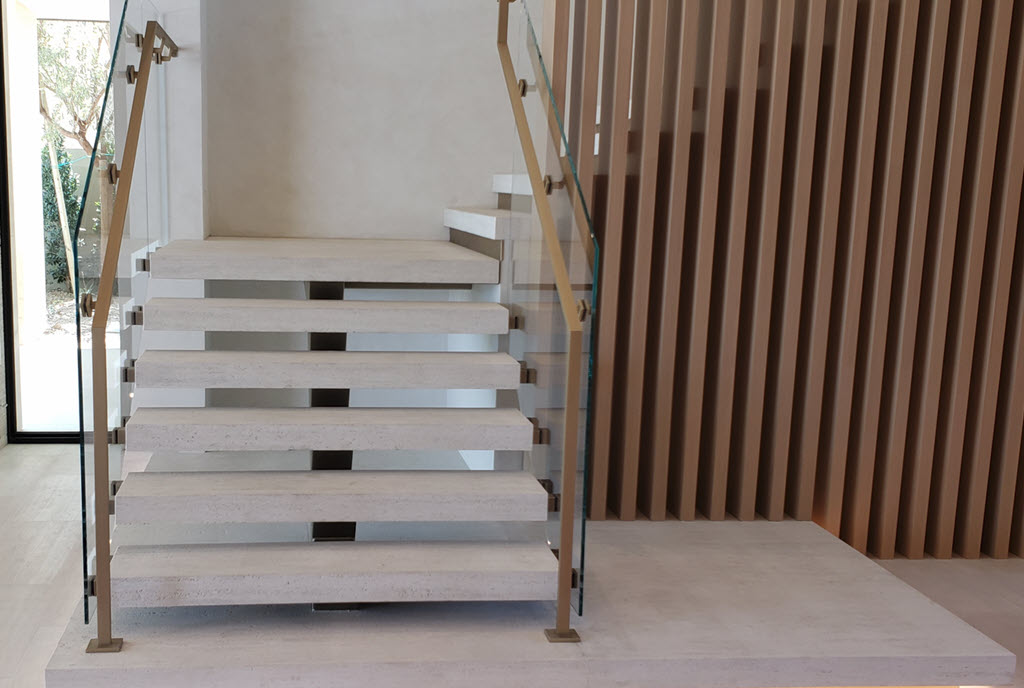 Slat walls offer a modern design style and pair well with this floating stair with open risers. The handrails are brass and traverse up the stairs and along the slat wall. Complements by a glass railing that adds luxury to the interior design of the space.