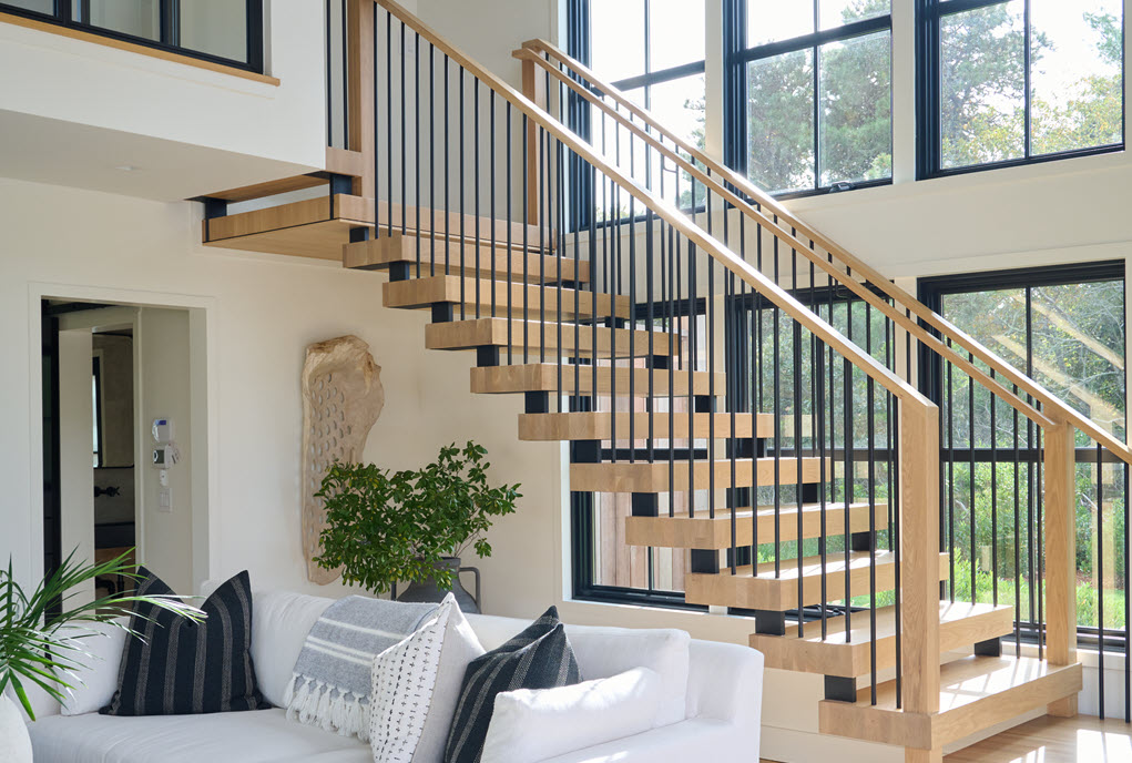 Window wall featuring black framed windows from floor to ceiling and white walls create a contrast with the spindle railing with white oak treads, landings and hand rails.