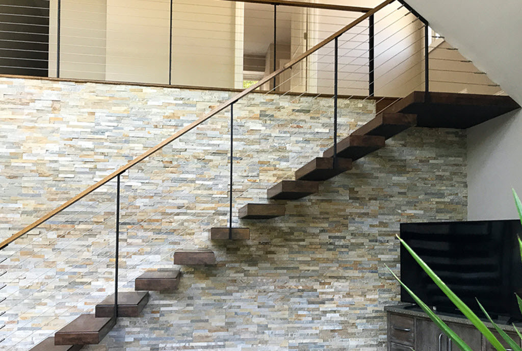 Cantilever Stair with vertical stacked stone wall. The stairs were designed to have the stringer hidden within the wall and the wood treads appear to float up the feature wall. The cable railing allows for an unobstructed view of the wall.