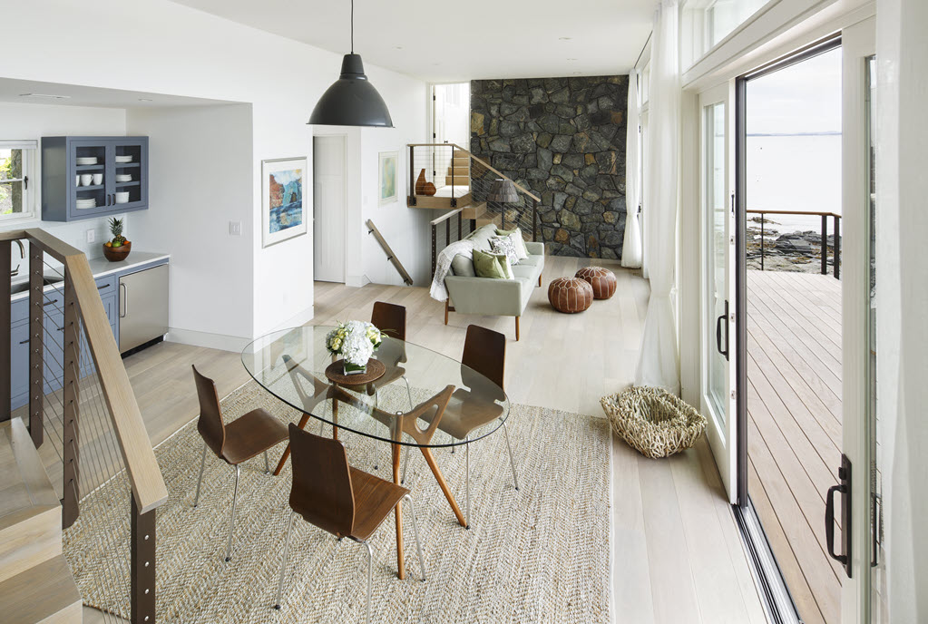 A modern contemporary home with clean lines contrasts the visual elemnets with a dark round stone wall. The glass stair railing allows for a seamless view of the feature wall