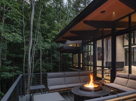 Ithaca cable railings wrap a modern deck with round fire pit and cozy furniture. The home has modern lines with expansive glass windows.