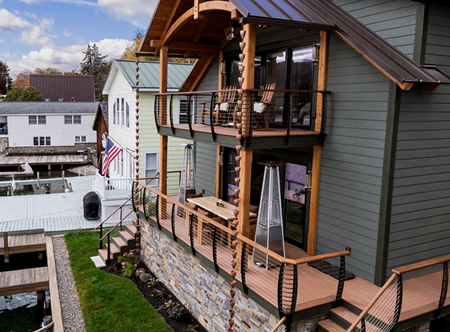 Post and beam home with fascia mounted Keuka style curved cable railing system fascia mounted on thedecks, exterior stairs and walkways. The home features warm earth tones with a stone wall.