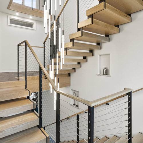 Light wood treads and handrails on a modern luxury staircase that has a black zig zag stringer slicing through the treads. Pendant lighting flows from the ceiling down the middle of the stairs.