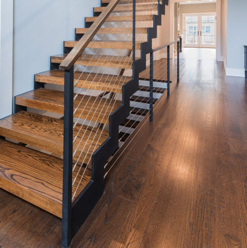 Black zig zag double stringer stair with red oak treads and cable railings in a room iwth matchin floors and natural light.
