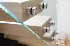 Glass railing close up with white oak wood treads and glass clamps connecting the glass railing to the staircase