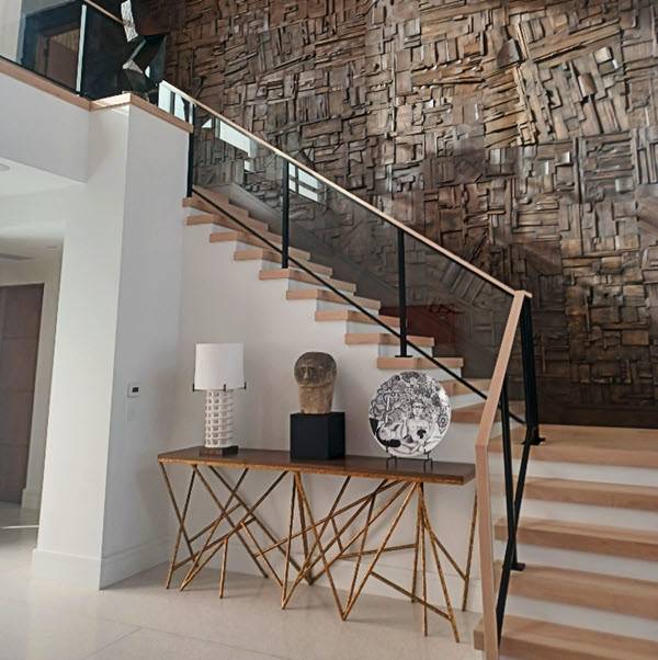 Black metal posts frame the glass on a staircase and balcony. The wood treads match the wood top rail that waterfalls down the tront of the handrail. The staircase perfectly complements the rustic wood wall design.