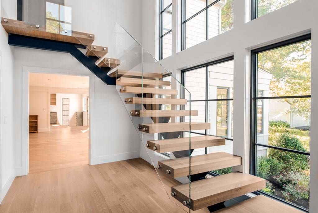 Floating Stairs with Glass Balustrade and white oak treads. The glass railing connects to the end of the treads creating a seamless appearance. The staircase floats up adjacent to a window wall allowing light to flow throughout the space