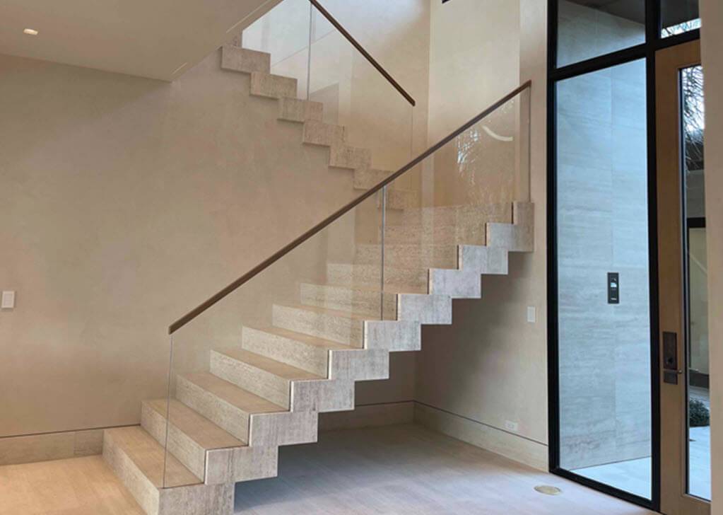 Glass railing on zig zag stairs with hidden glass attachments. The steel support structure for the stairs is concealed within the travertine stone creating a floating effect.