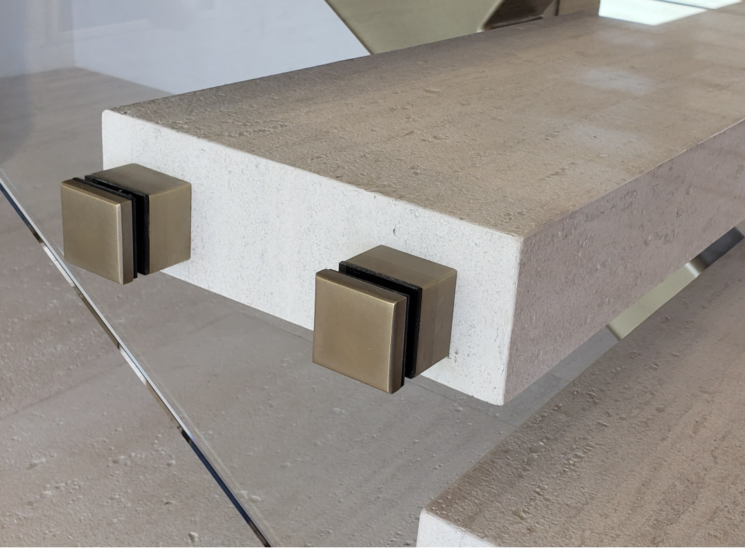 Close up of travertine stair tread with glass railing and square brass standoffs
